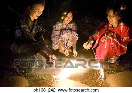 Stock Image - Three women playing with sparklers at night. Fotosearch