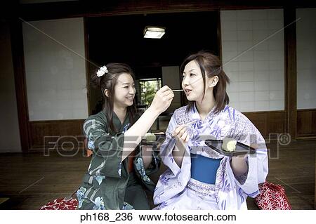 Stock Photograph - Two women in kimono having food by the corridor. Fotosearch