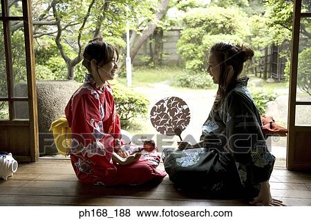 Stock Photo - Two women in kimono sitting by the corridor. Fotosearch