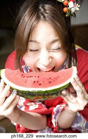 Stock Photo - Woman in kimono biting into water melon, close-up. Fotosearch
