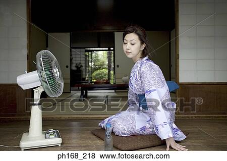 Stock Photo - Woman in kimono cooling herself in front of electric fan. Fotosearch