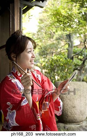 Stock Image - Woman in kimono holding a paintbrush and book. Fotosearch