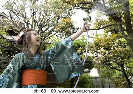 Stock Image - Woman in kimono watering the plants. Fotosearch