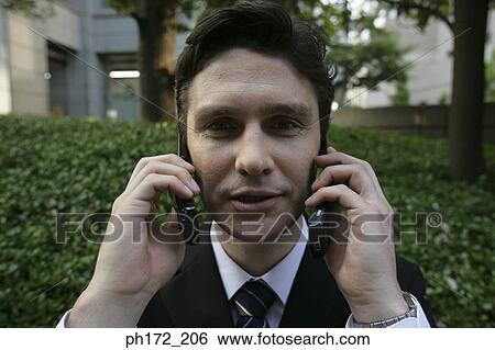 Businessman holding two mobile phones to his ears View Large Photo Image Stock Photograph - Businessman holding two mobile phones to his ears. Fotosearch