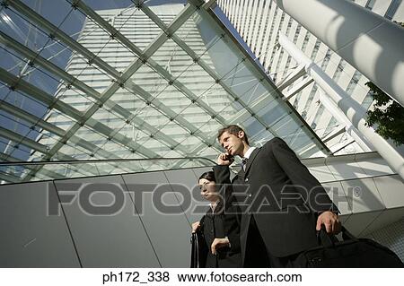 Male executive holding mobile phone with female executive standing next to him, low angle view View Large Photo Image Stock Photo - Male executive holding mobile phone with female executive standing next to him, low angle view. Fotosearch