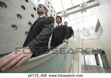 Three businessmen on escalator, close-up View Large Photo Image Stock Photo - Three businessmen on escalator, close-up. Fotosearch