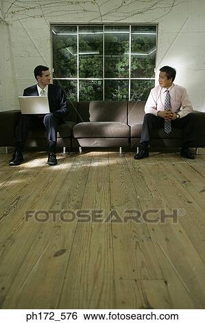 Two business men sitting on couch, looking at each other View Large Photo Image Stock Photograph - Two business men sitting on couch, looking at each other. Fotosearch