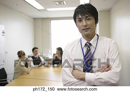 Male executive standing in board room with colleagues in background View Large Photo Image Stock Image - Male executive standing in board room with colleagues in background. Fotosearch