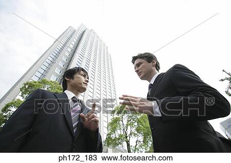 Two male executives standing by the sidewalk, low angle view View Large Photo Image Stock Image - Two male executives standing by the sidewalk, low angle view. Fotosearch