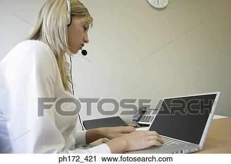 Female executive wearing headset and working on laptop View Large Photo Image Stock Image - Female executive wearing headset and working on laptop. Fotosearch