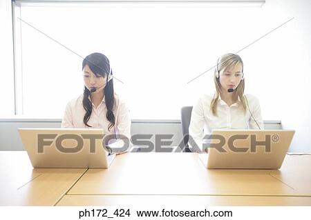 Two female executives wearing headsets and working on laptops View Large Photo Image Picture - Two female executives wearing headsets and working on laptops. Fotosearch