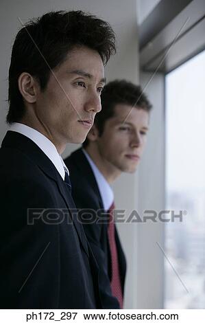 Two male executives looking out of window View Large Photo Image Stock Photo - Two male executives looking out of window. Fotosearch