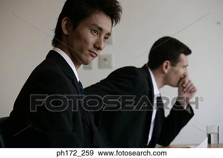 Stock Photo - Two male executives sitting in board room. Fotosearch
