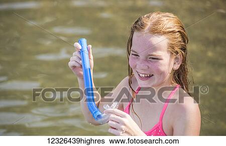 Stock Photograph - A 10-year-old Caucasian girl with red hair plays with a snorkel while swimming in Seneca Lake in upstate New York; Dresden, New York, United States of America. Fotosearch