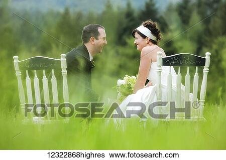 A bride and groom sit side by side in chairs in a grass field, talking and laughing together; Oregon, United States of America View Large Photo Image Stock Photograph - A bride and groom sit side by side in chairs in a grass field, talking and laughing together; Oregon, United States of America. Fotosearch
