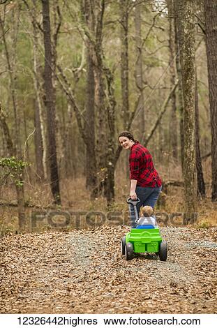 A Caucasian mother wearing a black and plaid shirt pulls her one-year old son in a green wagon on a gravel road covered with dead leaves; New Hill, North Carolina, United States of America View Large Photo Image Stock Photograph - A Caucasian mother wearing a black and plaid shirt pulls her one-year old son in a green wagon on a gravel road covered with dead leaves; New Hill, North Carolina, United States of America. Fotosearch