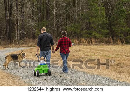 A caucasian mother with brown curly hair wearing a black and red plaid shirt and a caucasian father wearing a black shirt pull their one-year-old son in a green wagon on a gravel road with their German Shepard following along; New Hill, North... View Large Photo Image Stock Photograph - A caucasian mother with brown curly hair wearing a black and red plaid shirt and a caucasian father wearing a black shirt pull their one-year-old son in a green wagon on a gravel road with their German Shepard following along; New Hill, North.... Fotosearch