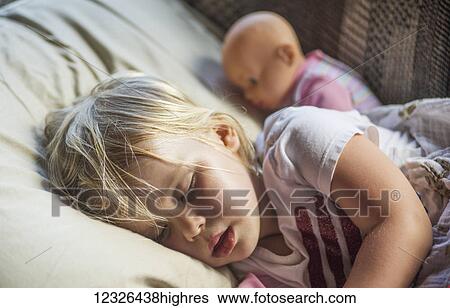 Stock Photograph - A caucasian toddler with blond hair naps with her doll; Penn Yan, New York, United States of America. Fotosearch