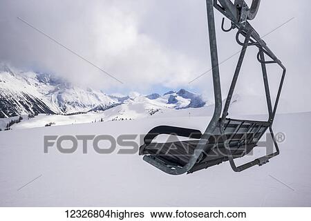 Stock Photograph - A chairlift over the snow with a view of the snow covered Canadian Rocky mountains in a ski resort; Whistler, British Columbia, Canada. Fotosearch