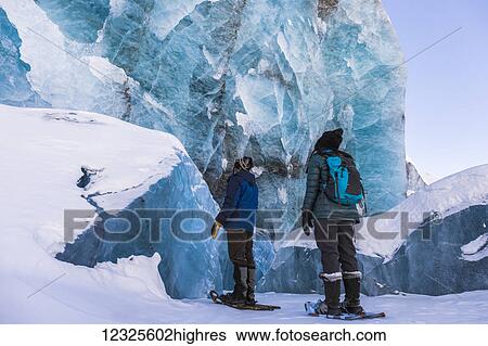 A couple of snowshoers examine a large blue wall of ice with several collapsed pieces of ice at the bottom at the terminus of Canwell Glacier in the Alaska Range; Alaska, United States of America View Large Photo Image Stock Photograph - A couple of snowshoers examine a large blue wall of ice with several collapsed pieces of ice at the bottom at the terminus of Canwell Glacier in the Alaska Range; Alaska, United States of America. Fotosearch