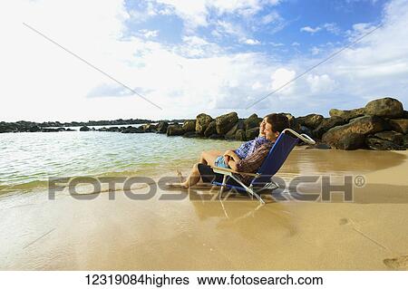 Stock Photograph - A couple sits in a beach chair together facing the ocean on Lydgate Beach; Kauai, Hawaii, United States of America. Fotosearch