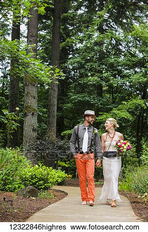 Stock Photograph - A couple walks in bare feet down a paved path holding hands and laughing; Oregon, United States of America. Fotosearch