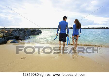 Stock Photograph - A couple walks into the water from Lydgate Beach holding flippers and s0rkeling gear; Kauai, Hawaii, United States of America. Fotosearch