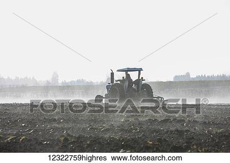 Stock Photograph - A farmer ploughing a field with a tractor and plough. Fotosearch