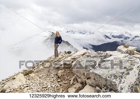 Stock Photograph - A female hiker reaches the mountain summit and poses for a photo of the accomplishment at Kicking Horse Mountain in the Rocky Mountains; British Columbia, Canada. Fotosearch