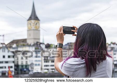 Stock Photograph - A female tourist takes a landscape photo with her phone while on vacation; Zurich, Switzerland. Fotosearch