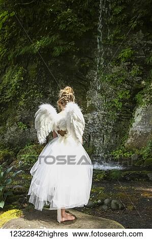 A girl with blond hair wearing an angel costume with feather wings stands at the edge of a tranquil pool; Oregon, United States of America View Large Photo Image Stock Photograph - A girl with blond hair wearing an angel costume with feather wings stands at the edge of a tranquil pool; Oregon, United States of America. Fotosearch