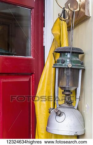 Stock Photograph - A lantern and yellow rain jacket hang beside a red door; Yorkshire, England. Fotosearch