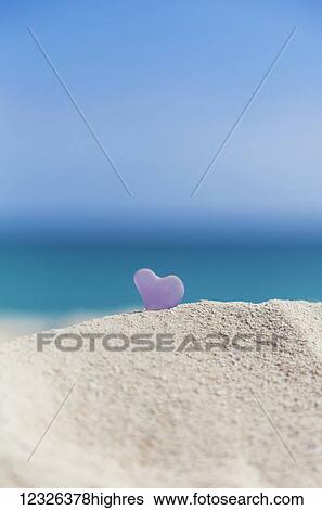 Stock Photograph - A lavender heart shaped sea glass in the sand at the beach; Honolulu, Oahu, Hawaii, United States of America. Fotosearch