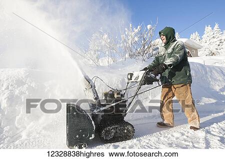 Stock Photograph - A man happily using his snowblower in front of his house; Alaska, United States of America. Fotosearch