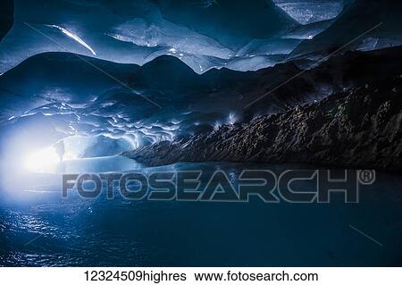Stock Photograph - A man is silhouetted by the entrance to a dark ice cave within Augustana Glacier in the Alaska Range; Alaska, United States of America. Fotosearch