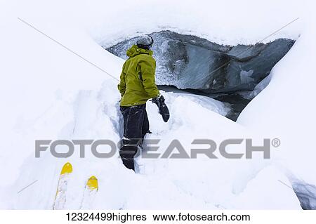 Stock Photograph - A man observes a stream emanating from beneath Fels Glacier in the Alaska Range in January; Alaska, United States of America. Fotosearch