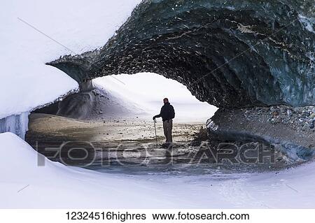 Stock Photograph - A man on snowshoes stands beneath the ice of Canwell Glacier in the Alaska Range in winter; Alaska, United States of America. Fotosearch