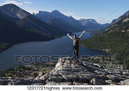 Stock Photograph - A man stands on a rocky ridge overlooking a lake and mountains in Waterton Lakes National Park; Alberta, Canada. Fotosearch