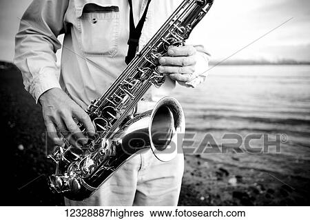 Stock Photograph - A man stands playing a saxophone on the beach at the water's edge; Alaska, United States of America. Fotosearch