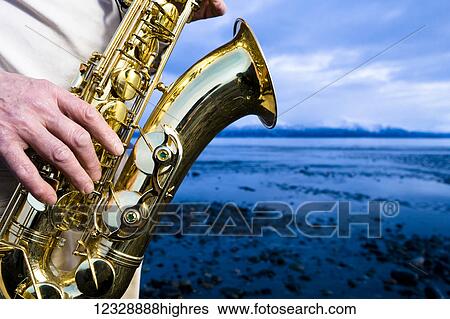 A man stands playing a saxophone on the beach at the water's edge; Alaska, United States of America View Large Photo Image Stock Photograph - A man stands playing a saxophone on the beach at the water's edge; Alaska, United States of America. Fotosearch