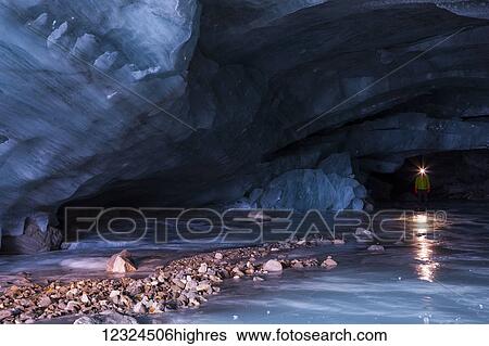 Stock Photograph - A man's headlamp reflects off the icy floor of a cavernous ice cave at the terminus of Augustana Glacier in the Alaska Range; Alaska, United States of America. Fotosearch