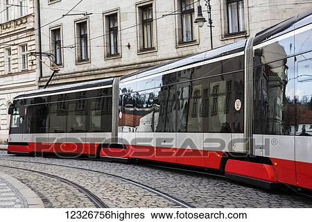 Stock Photograph - A modern electric train makes it's way over cobblestone streets; Prague, Czechia. Fotosearch