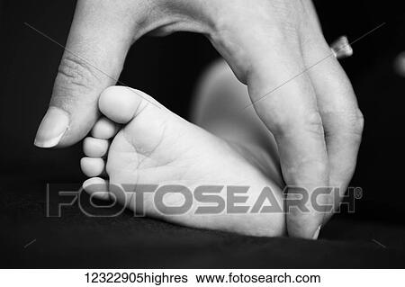 Stock Photograph - A mother touches her newborn's bare foot against a black background; Oregon, United States of America. Fotosearch