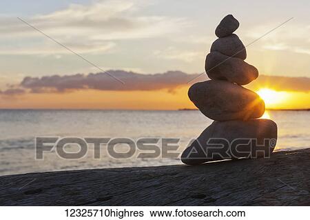 A pile of rocks balancing on the sand at the water's edge with the golden sun setting over the ocean; Honolulu, Oahu, Hawaii, United States of America View Large Photo Image Stock Photograph - A pile of rocks balancing on the sand at the water's edge with the golden sun setting over the ocean; Honolulu, Oahu, Hawaii, United States of America. Fotosearch