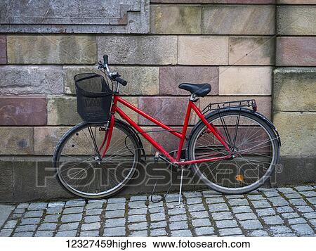 Stock Photograph - A red bicycle parked against a wall of stone blocks; Stockholm, Sweden. Fotosearch
