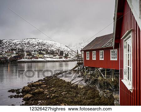 A red building along the water's edge with snow covered hills under a cloudy sky; Lofoten Islands, Nordland, Norway View Large Photo Image Stock Photograph - A red building along the water's edge with snow covered hills under a cloudy sky; Lofoten Islands, Nordland, Norway. Fotosearch