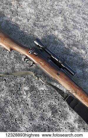 Stock Photograph - A rifle with telescope and strap used for a seal hunt laying on the ice; Alaska, United States of America. Fotosearch