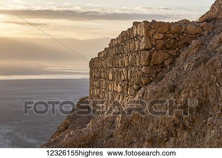 Stock Photograph - A rock wall along a cliff with a view of the Judaean Desert; South District, Israel. Fotosearch