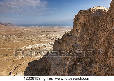 Stock Photograph - A rugged rock cliff and a view of the Judaean Desert, Dead Sea region; South District, Israel. Fotosearch