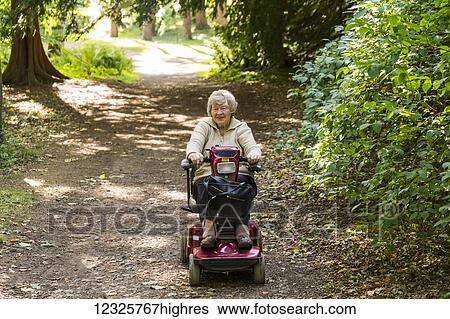 Stock Photograph - A senior woman rides a motorized wheelchair down a trail in a park; Yorkshire, England. Fotosearch